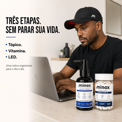 Homem usando o Boné LED .minox enquanto trabalha, com Minoxidil e Vitamina Capilar sobre a mesa
